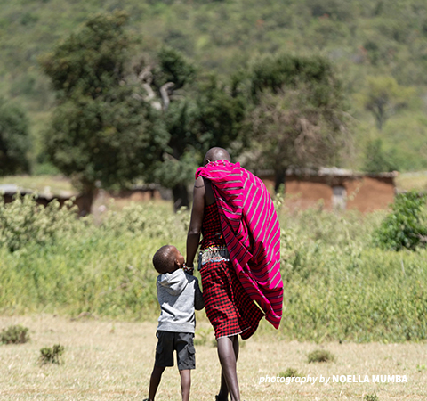 Adult and child walking in front of greenery.