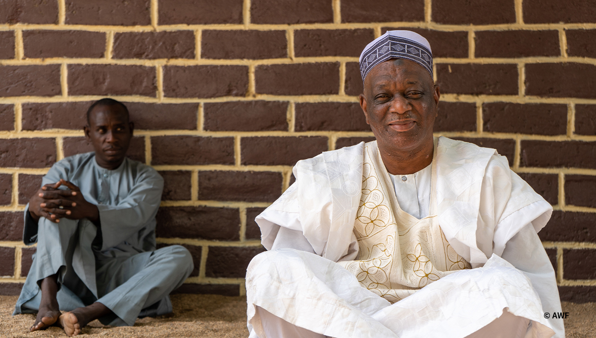 Medium shot of two men sitting in front of a brick wall.