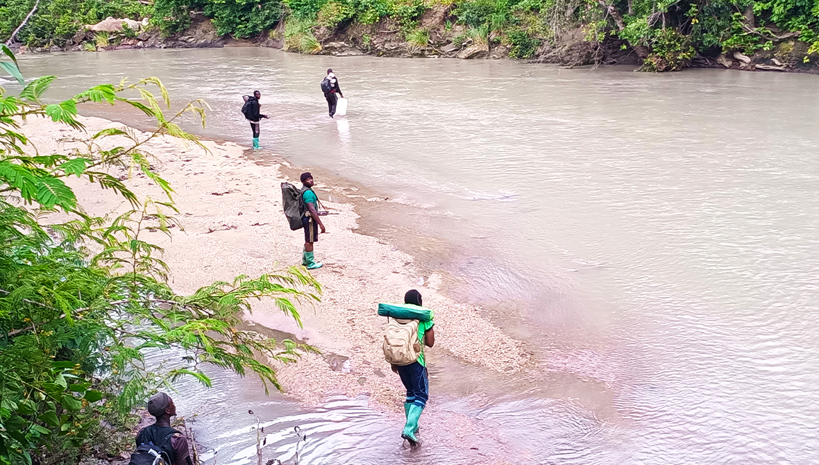 People in outdoor gear wade through a river.