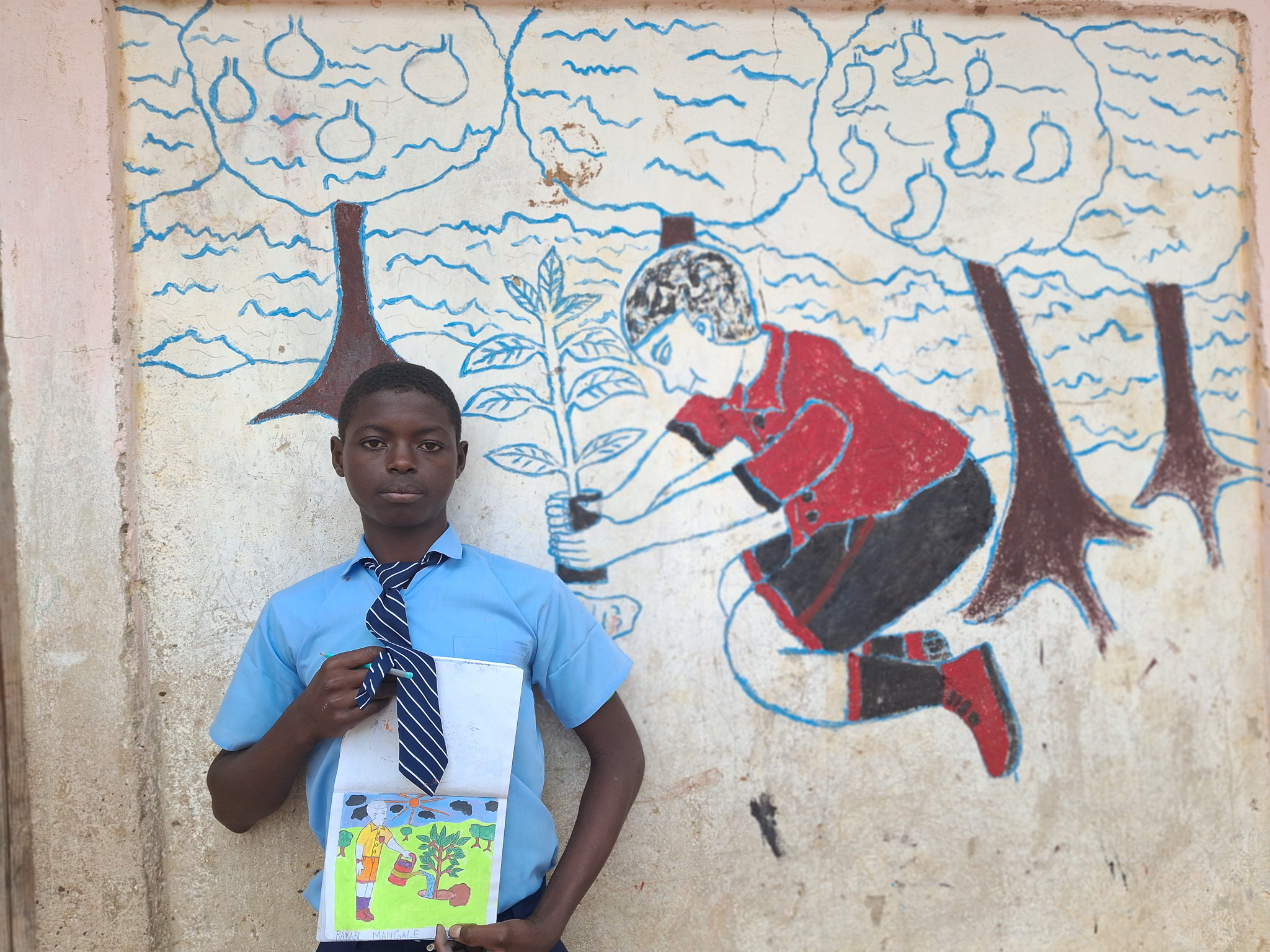 Bakari showcasing some of his pieces both in his drawing book and the wall art mural. 
