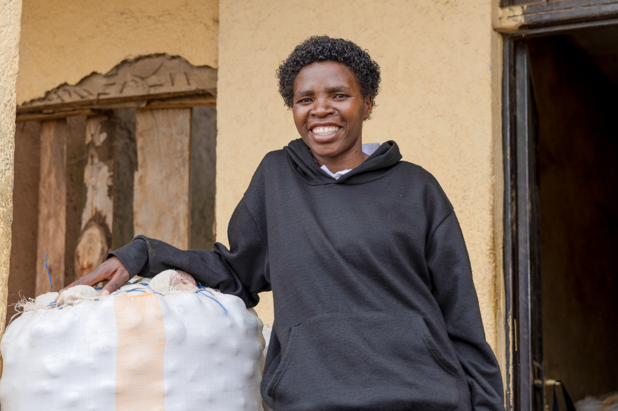 Mukarwego Agnes standing beside stored Irish potatoes, a key commodity in her agribusiness.