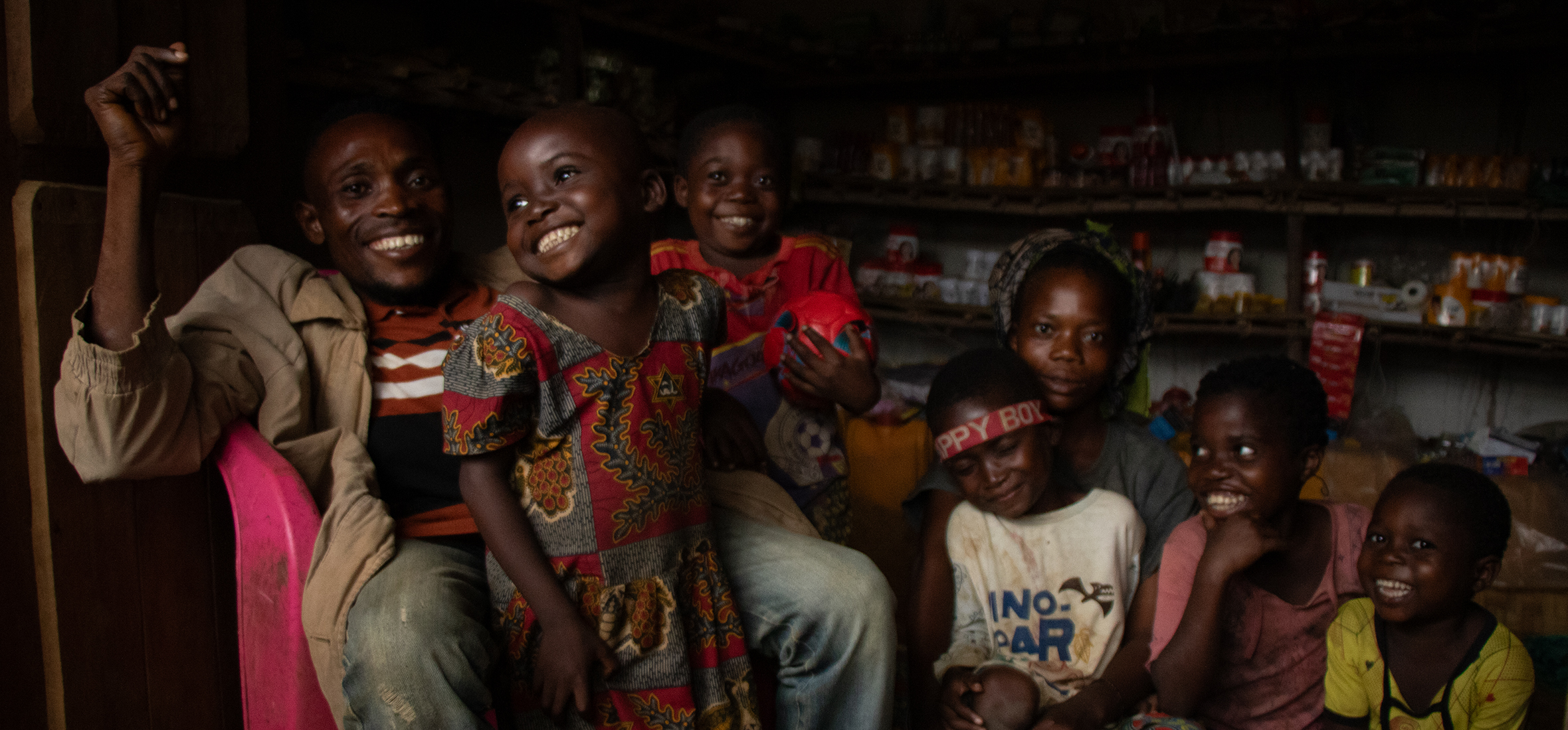 Nsembe Balombo Guy in his shop, surrounded by the joyful smiles of his family in Ilima village.