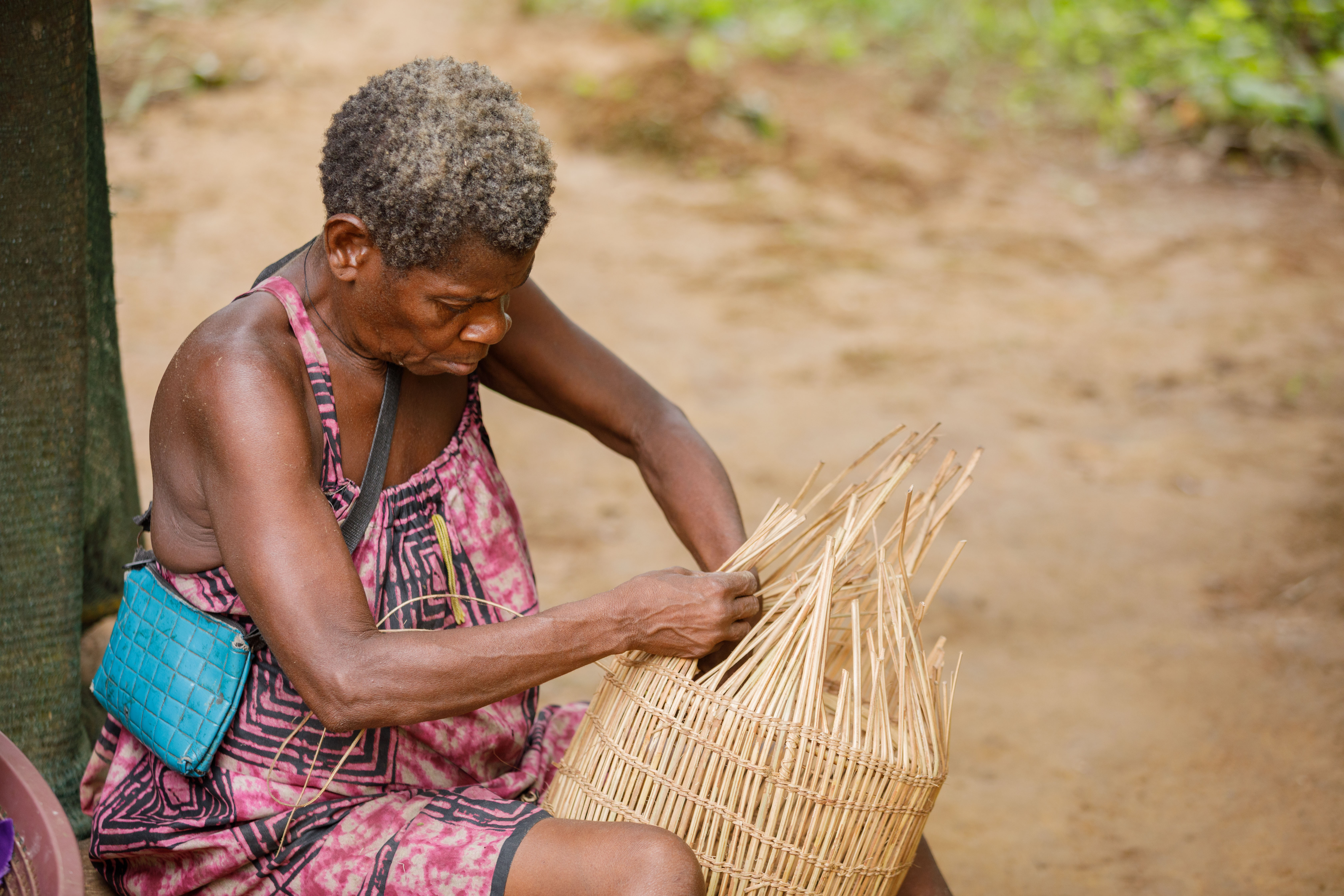 Mama Antoinette sits in front of her home weaving a basket, which will be used for fishing and to transport food. © Vanilla Boi Studios