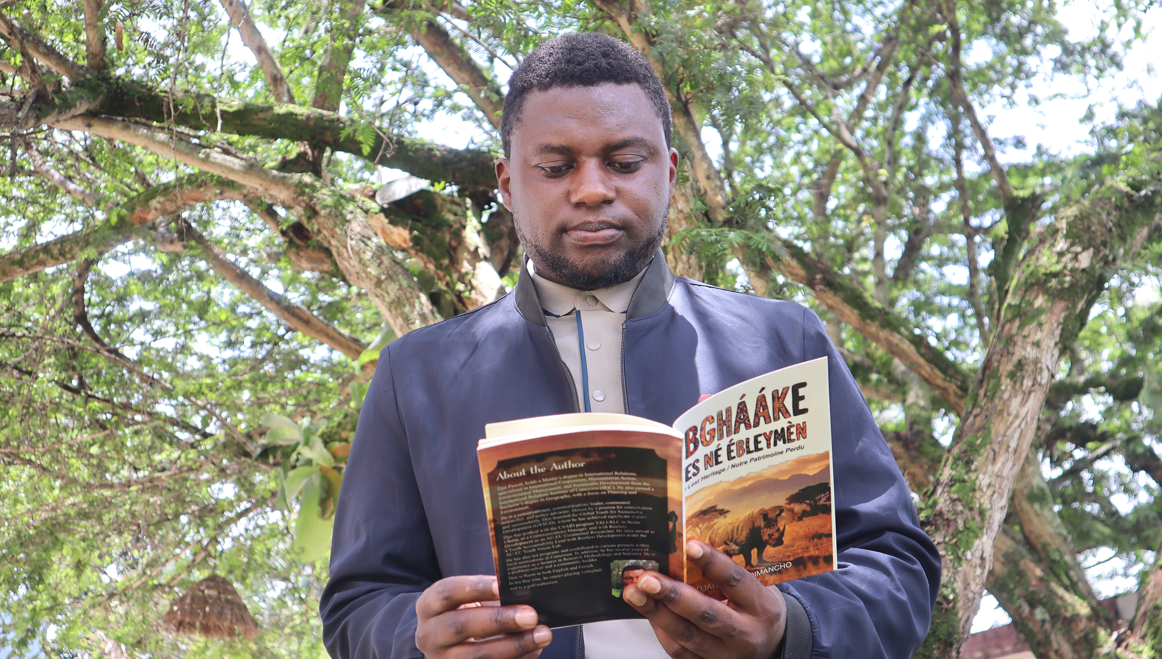 Djai Pascal holding his book Bghááke Es Né Ébleymèn (Our Lost Heritage / Notre Patrimoine Perdu), exploring the tragic history and legacy of Cameroon's extinct black rhinos.