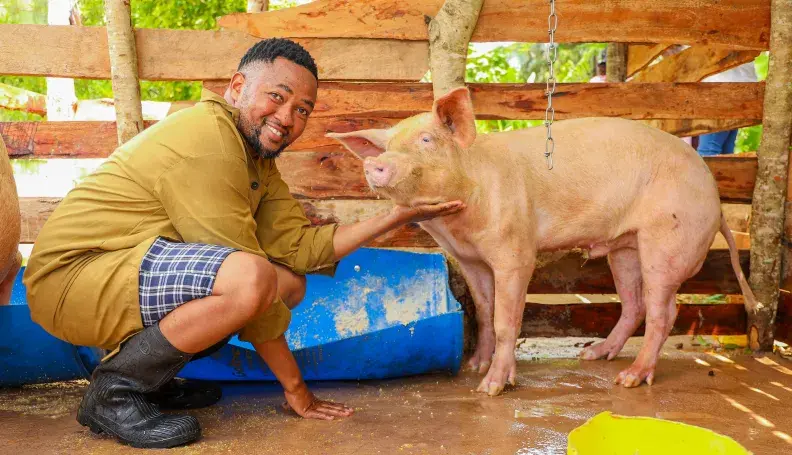 Hedlam Toli posing for a photo with his pig in a pig pen.