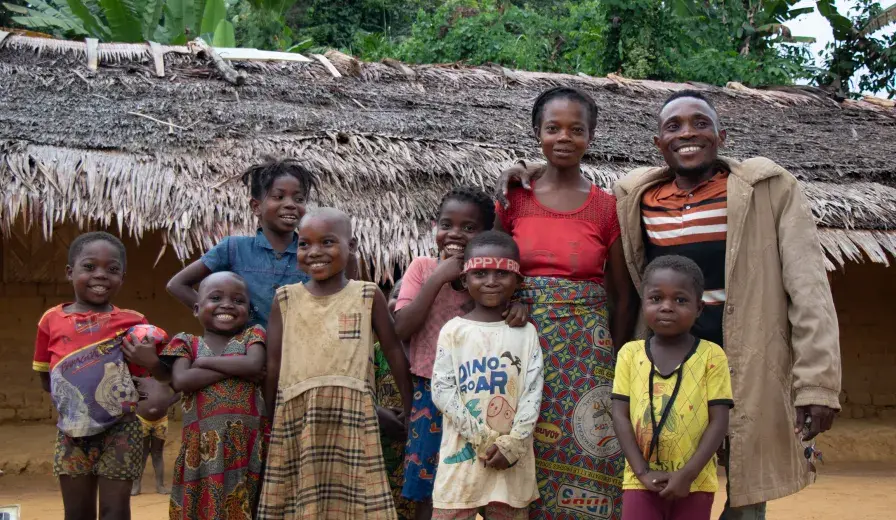 Nsembe Balombo Guy with his family and nephews in front of his home, a symbol of newfound stability and empowerment.