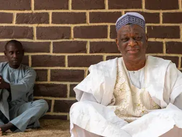Medium shot of two men sitting in front of a brick wall.