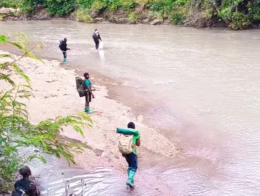 People in outdoor gear wade through a river.