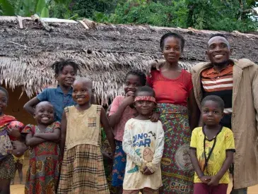 Nsembe Balombo Guy with his family and nephews in front of his home, a symbol of newfound stability and empowerment.
